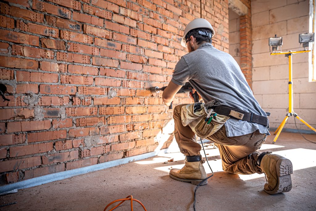 bauarbeiter bohrt mit schlagbohrer in die wand